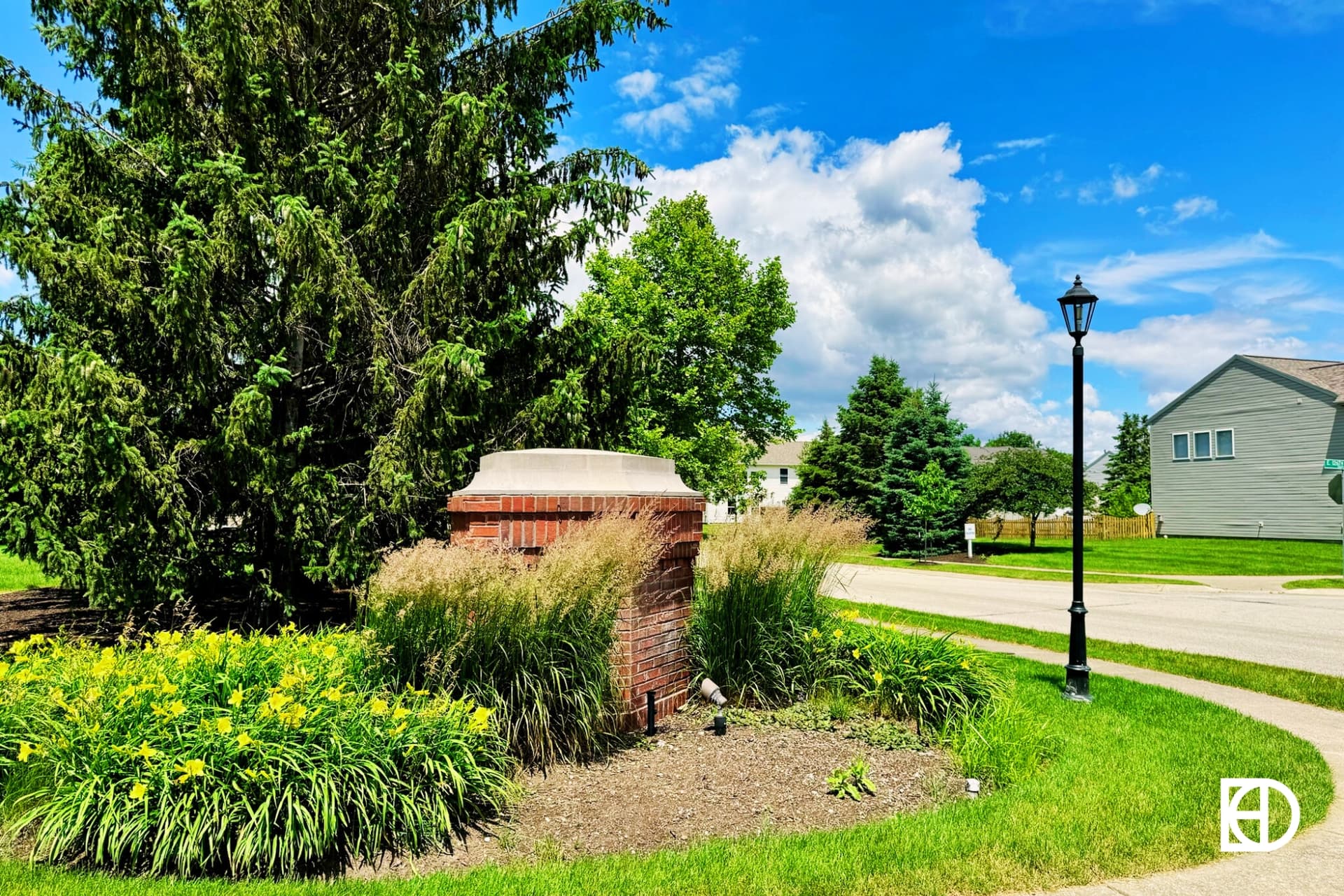 Photo of entrance to Plum Creek Farms with small brick sign, landscaping and trees.