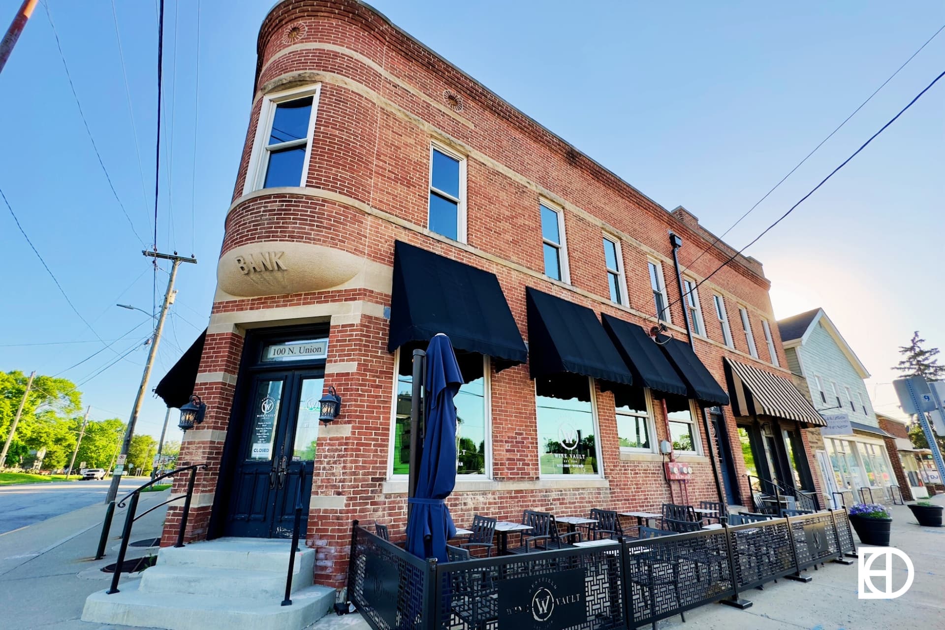 A historic red brick building with black awnings and outdoor seating, featuring a sign that reads BANK above the entrance.