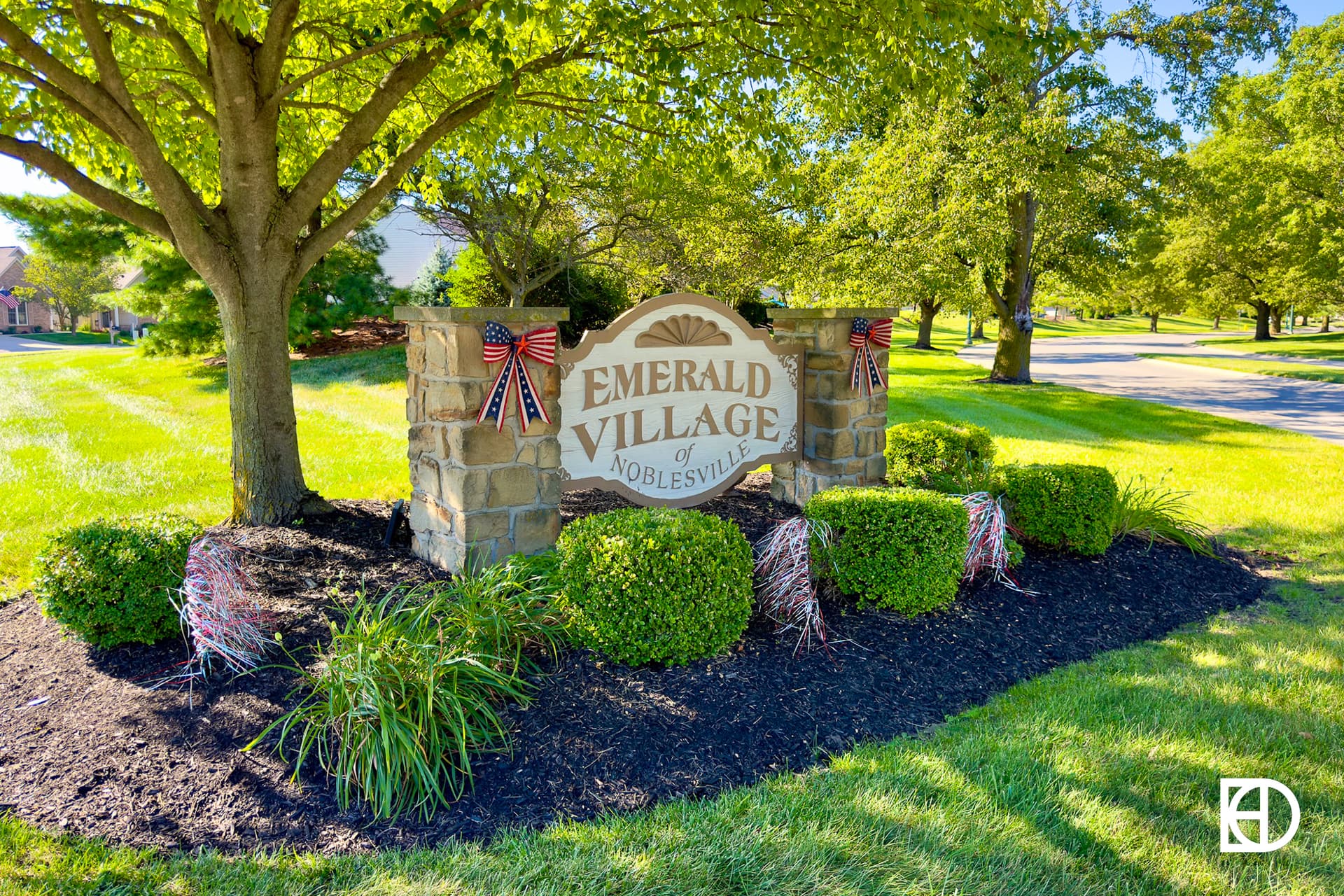 Stone entrance sign to Emerald Village, shaded by large trees and with landscaping around base.