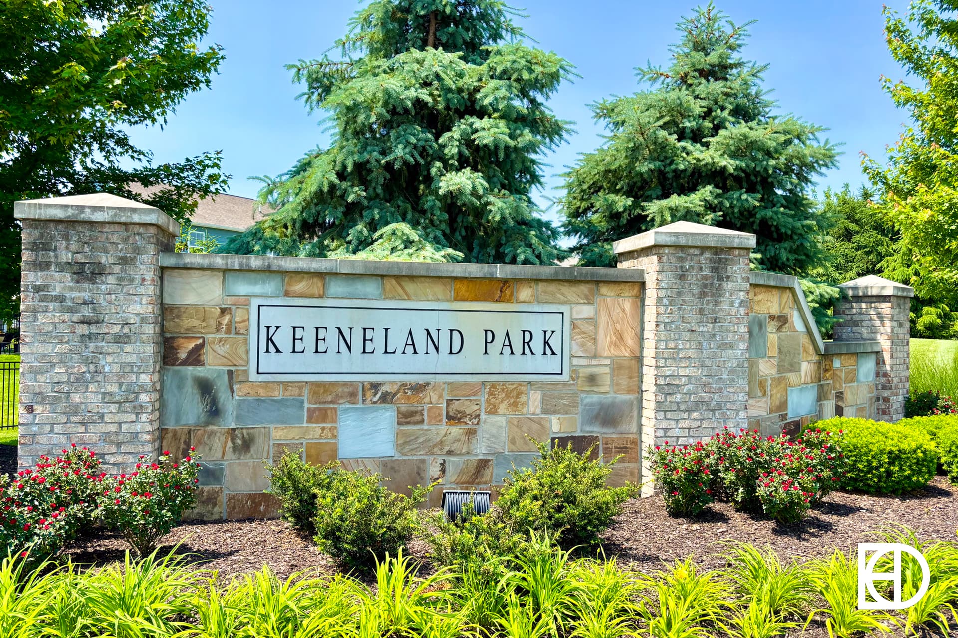 A brick and stone entrance sign reads “Keeneland Park,” surrounded by landscaping with bushes and evergreen trees.