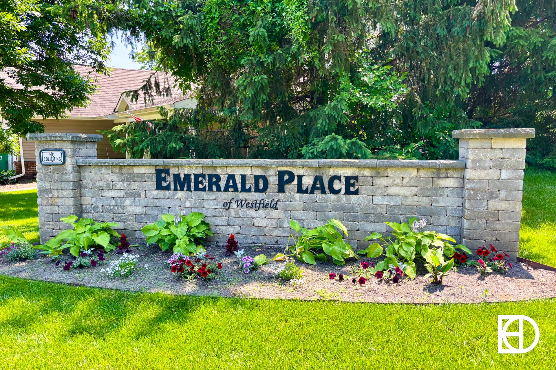 A stone sign reading Emerald Place of Westfield is surrounded by flowers and greenery, with a house and trees in the background.