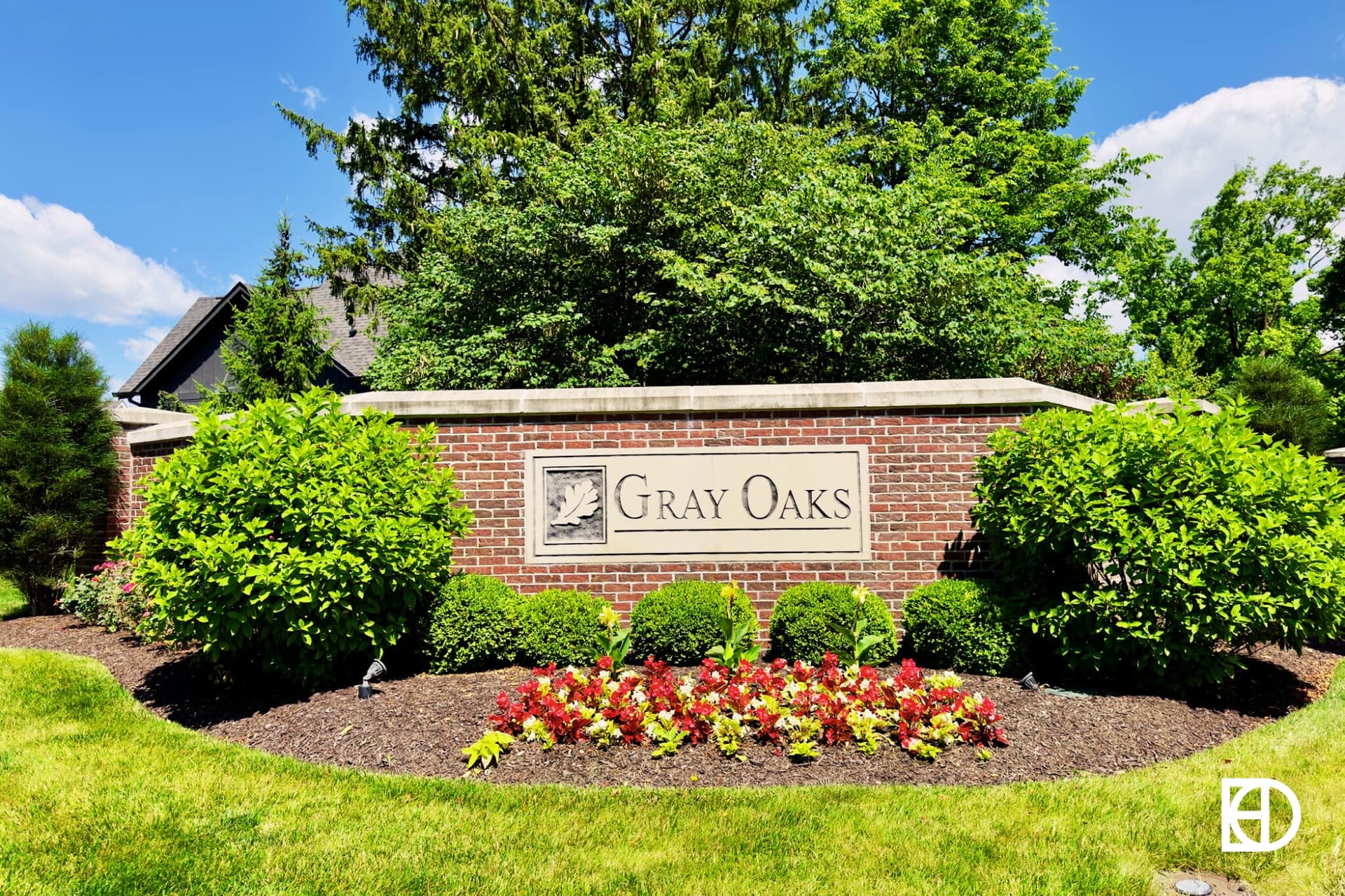 Photo of brick entrance sign with shrubs, flowers and trees behind.
