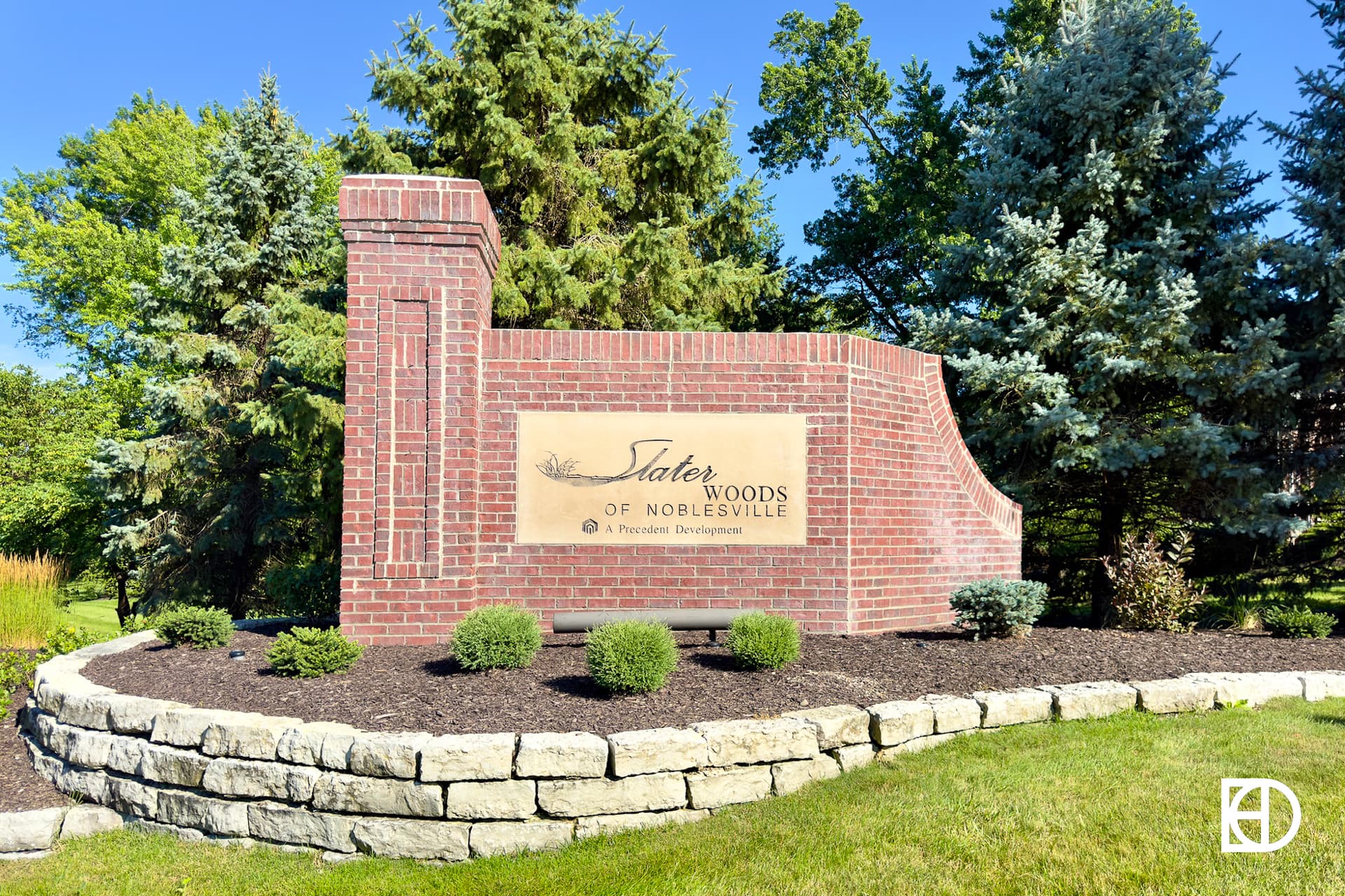 Brick entrance sign for Slater Woods of Noblesville, with stone surround and flanked by trees.