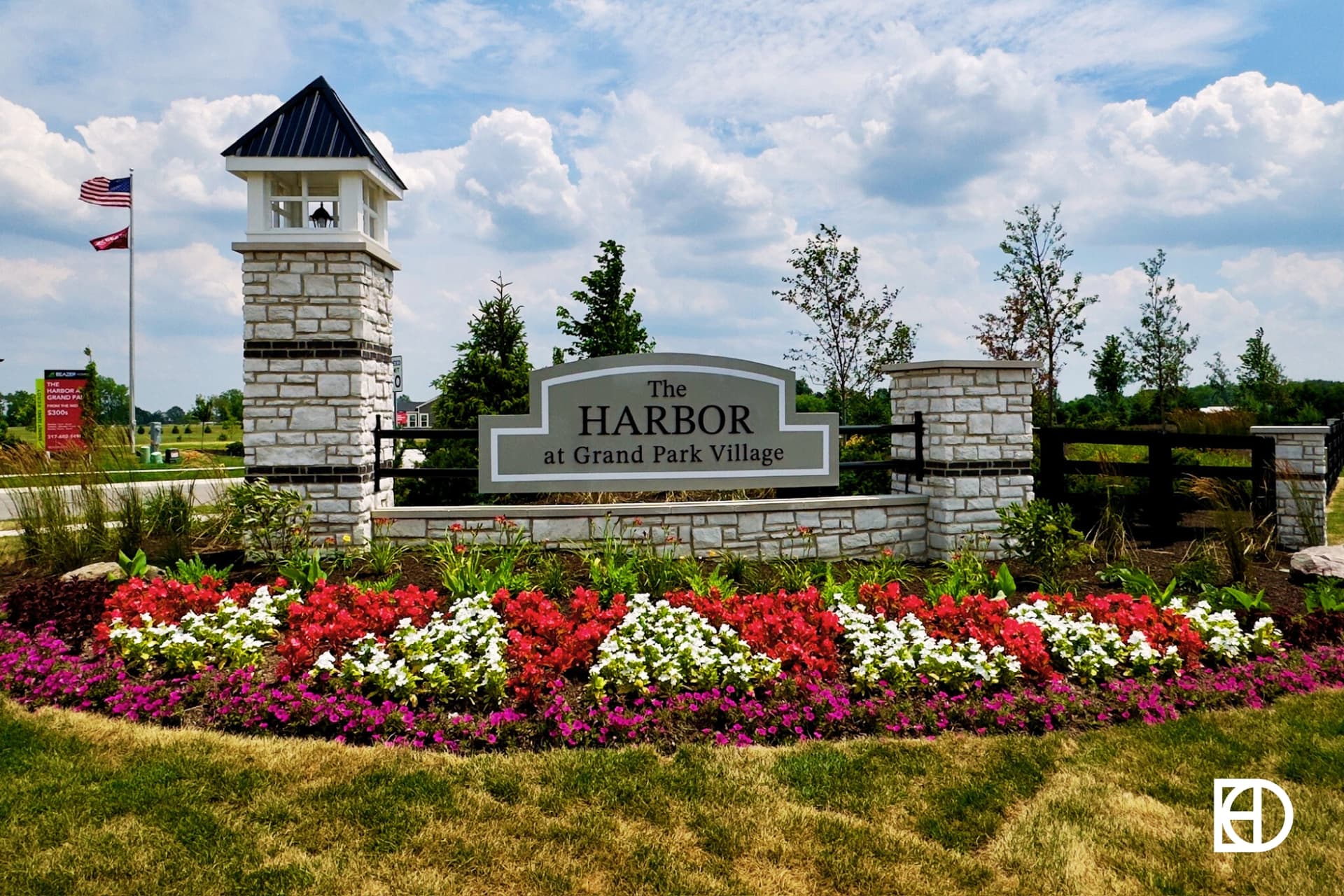 Neighborhood sign for Harbor at Grand Park Village with stone wall, column, wood fencing all surrounded by flowers in a large landscape bed.
