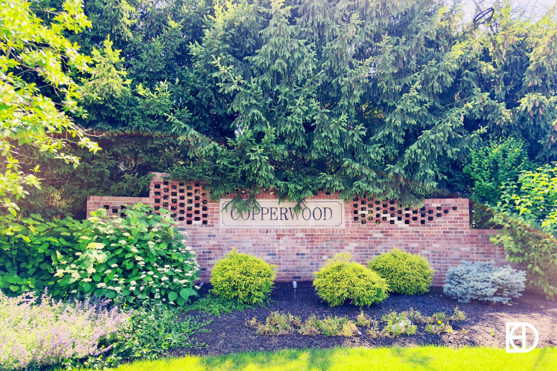 Brick entrance sign to Copperwood neighborhood with landscaping and large trees behind.