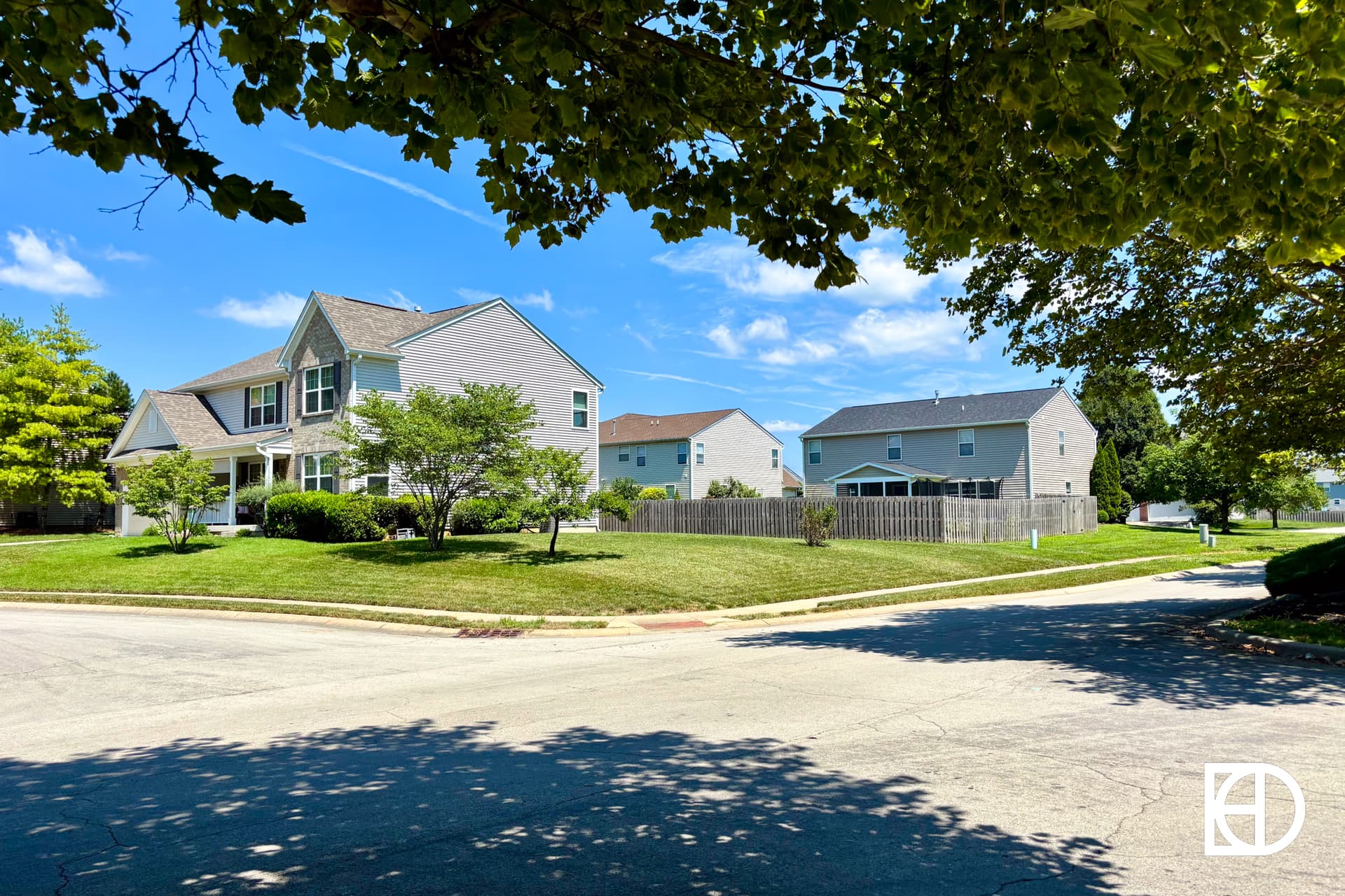 A stone entrance sign reads Briarwood Trace surrounded by green shrubs and plants, with a blue sky and a few clouds in the background.