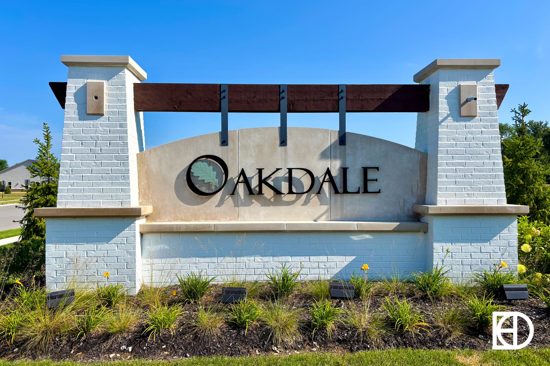 A large stone and brick sign with the word OAKDALE and a leaf logo, set in front of greenery and a clear blue sky.