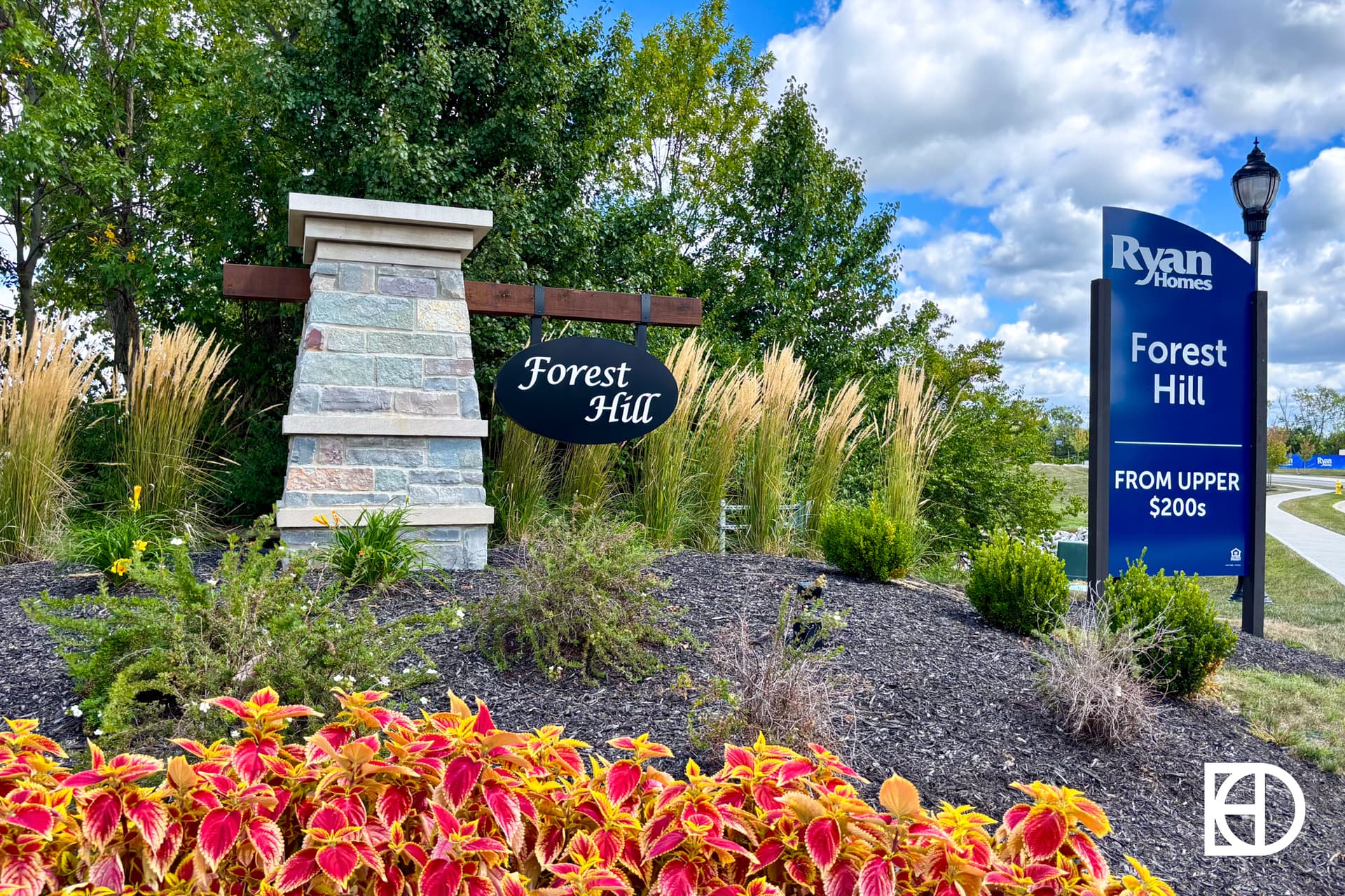 Entrance sign for Forest Hill neighborhood, with landscaping, ornamental grass, and a Ryan Homes sign stating homes available from the upper $200s. Trees and a partly cloudy sky are in the background.