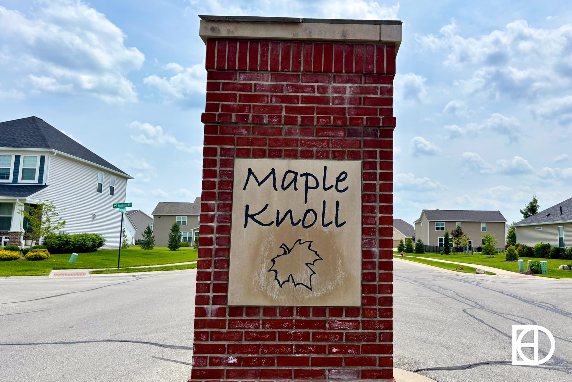 Brick entrance sign with “Maple Knoll” and a maple leaf symbol, located at the entrance of a suburban residential neighborhood.