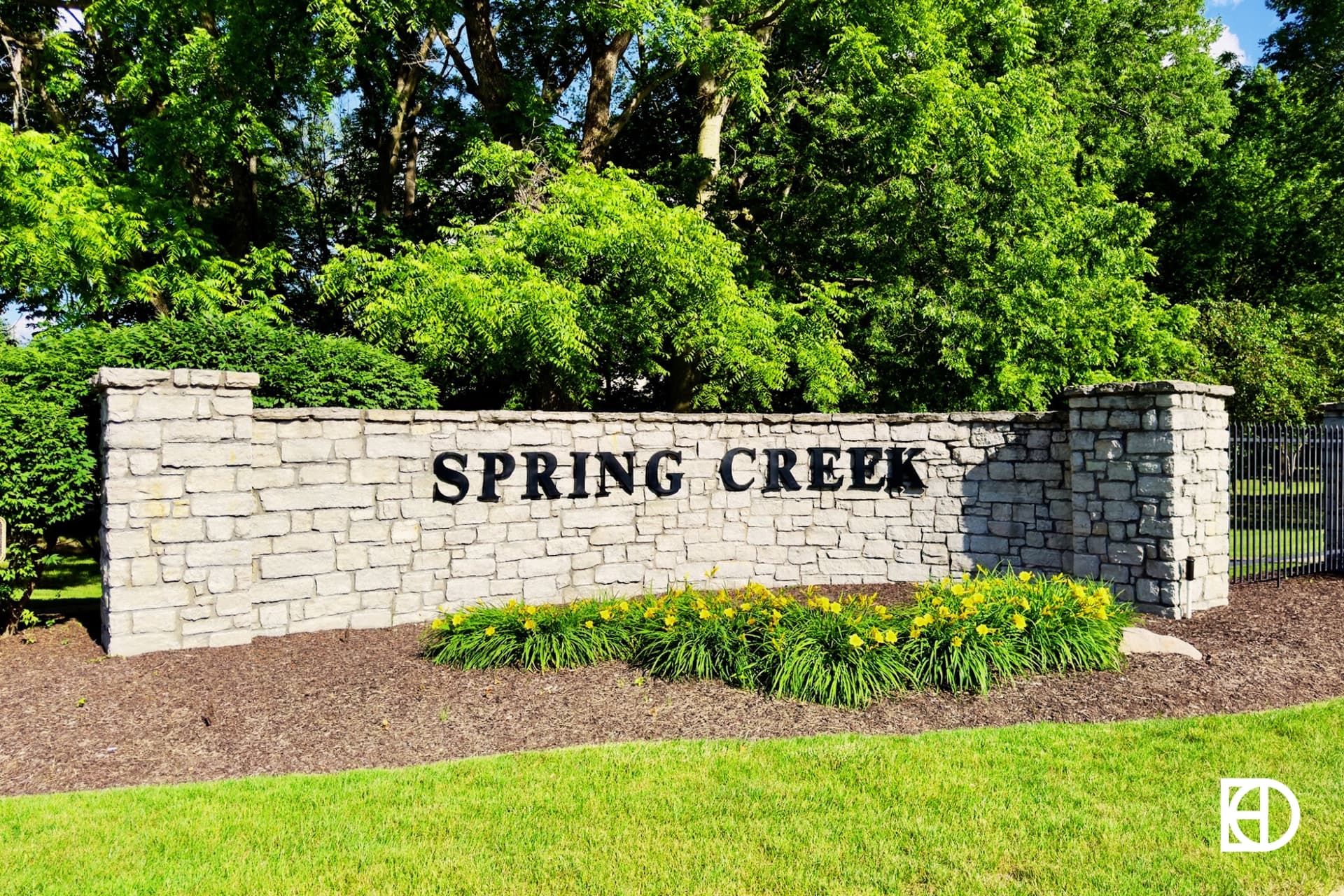 Stone half wall entrance sign with black letters for Spring Creek neighborhood.