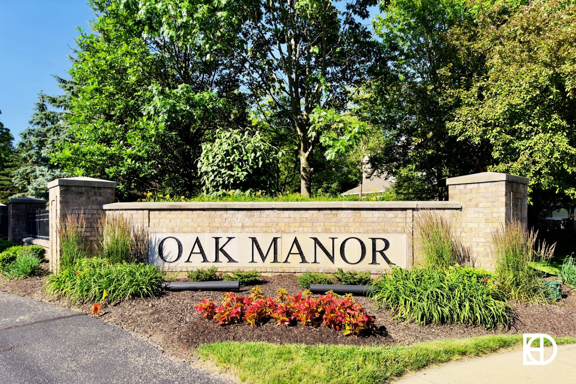 A brick entrance sign reads OAK MANOR surrounded by landscaped plants, shrubs, and trees.