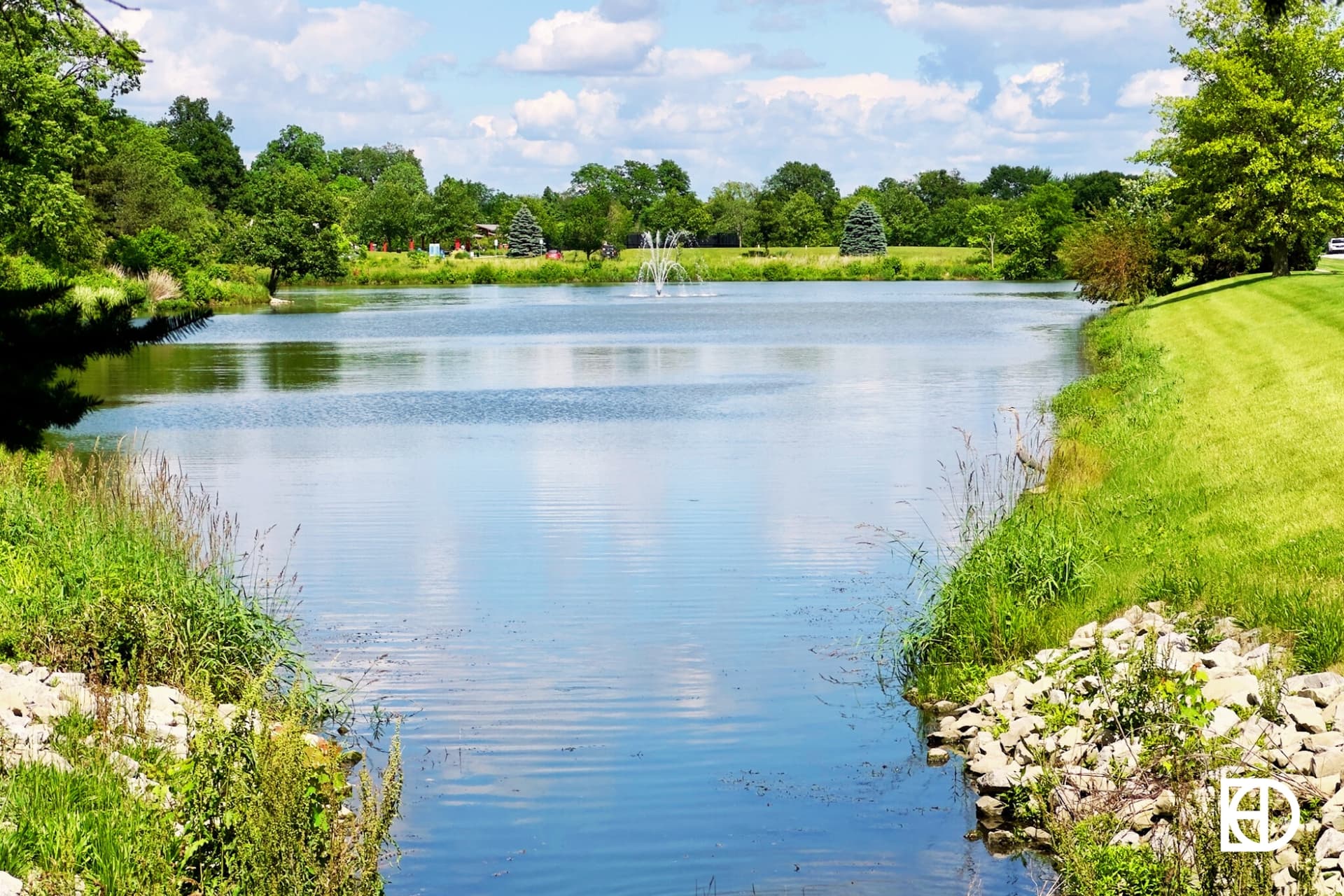 Photo overlooking pond with fountain, surrounded by greenspace and trees in Plum Creek North neighborhood.