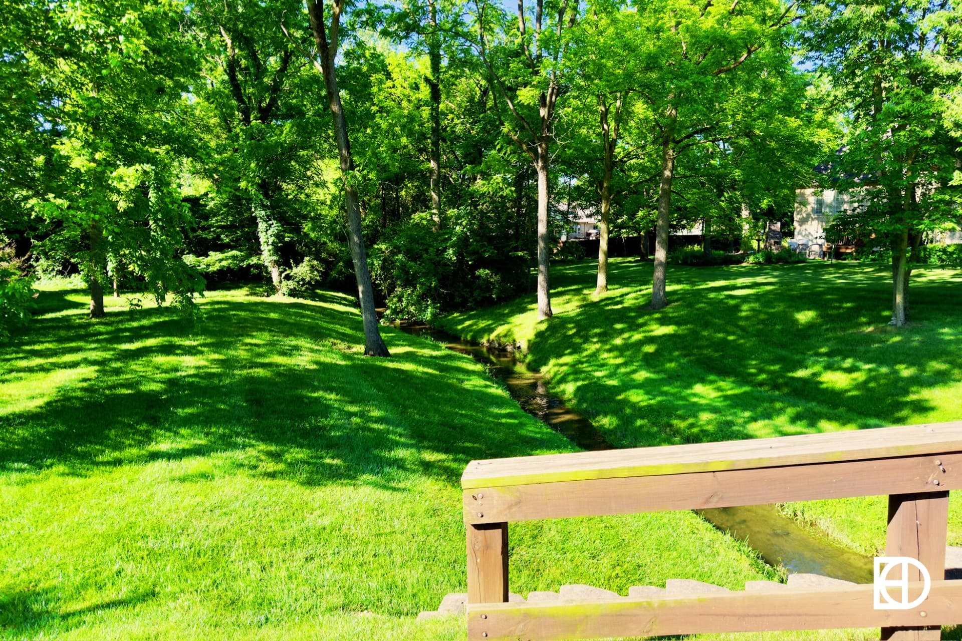 Photo of green space and small creek under bridge with trees in the background.