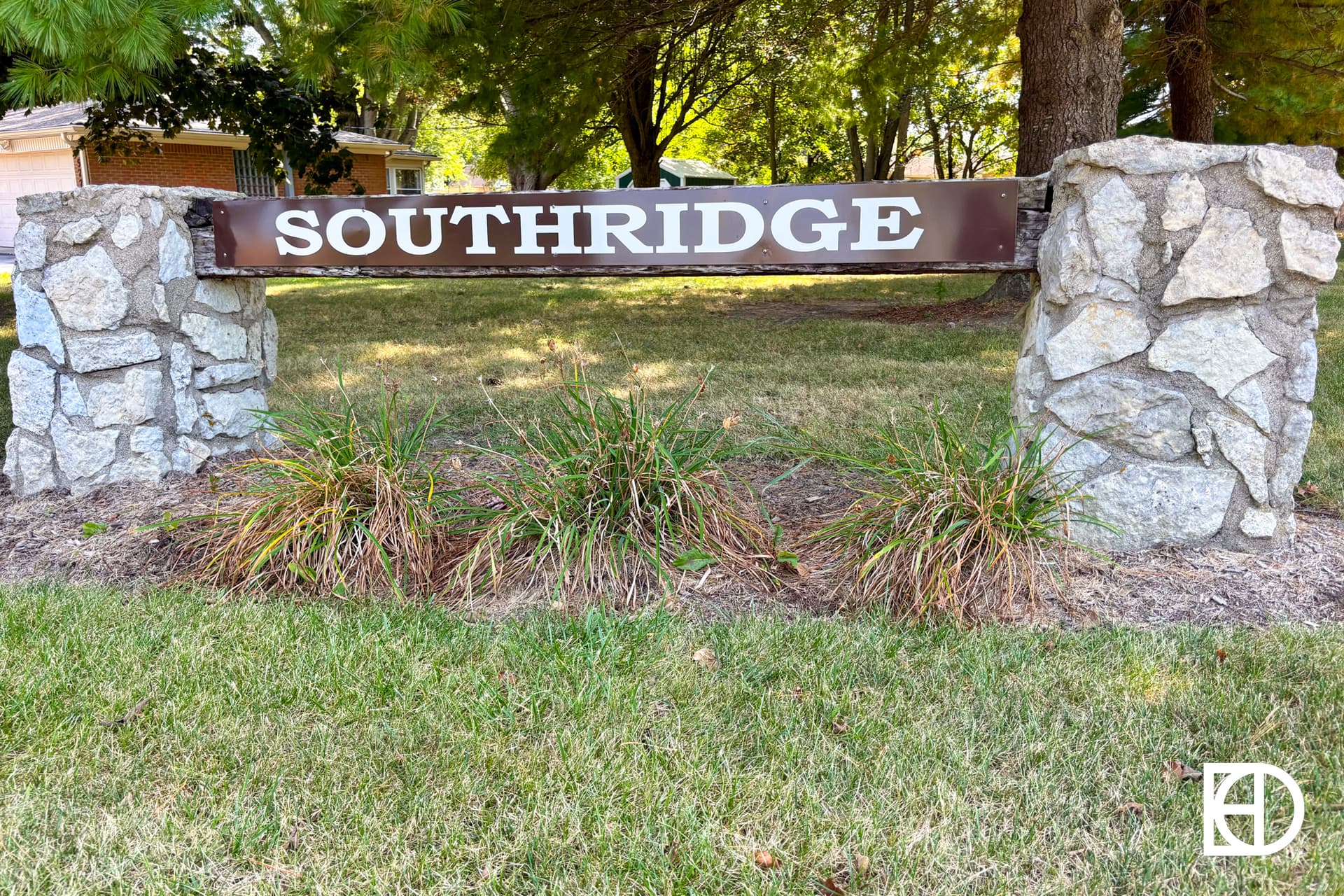 A brown and white sign reading SOUTHRIDGE is mounted between two stone pillars on a grassy lawn with trees and a house visible in the background.