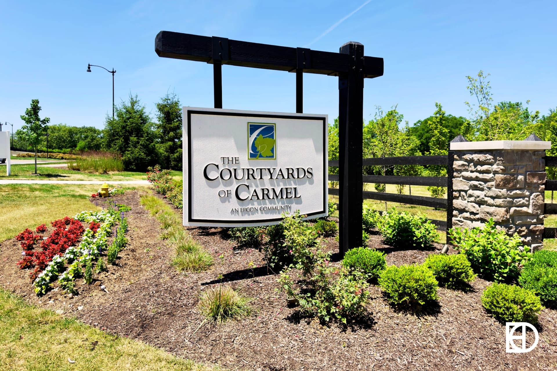 Hanging wood entrance sign for Courtyards of Carmel neighborhood, with landscaping and fencing creating an entrance to the neighborhood.