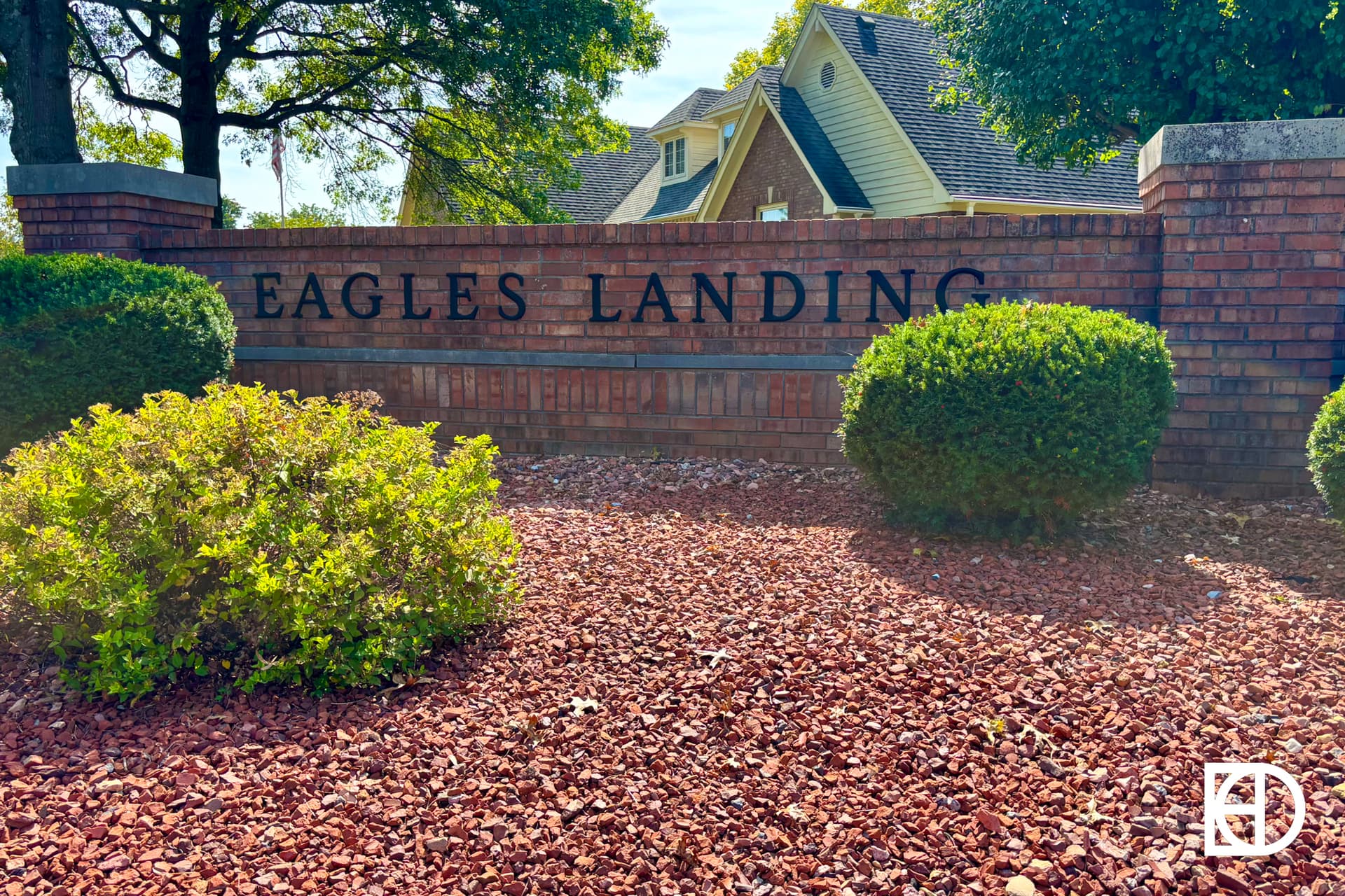 A brick sign reading Eagles Landing is surrounded by neatly trimmed bushes, red mulch, and trees. In the bottom right corner, there is a white KD logo.