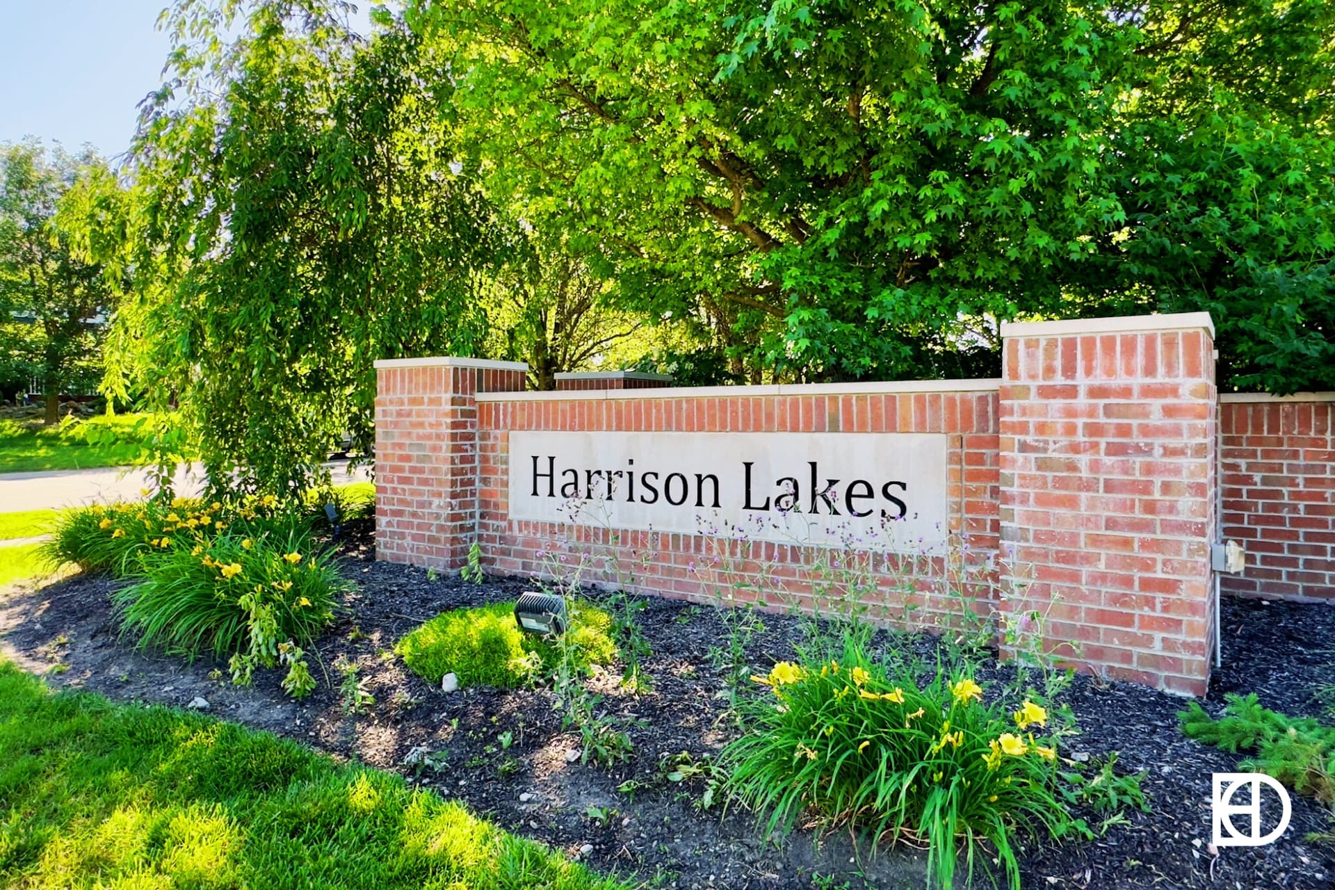 Exterior photo of Harrison Lakes, showing signage on small brick wall and landscaping