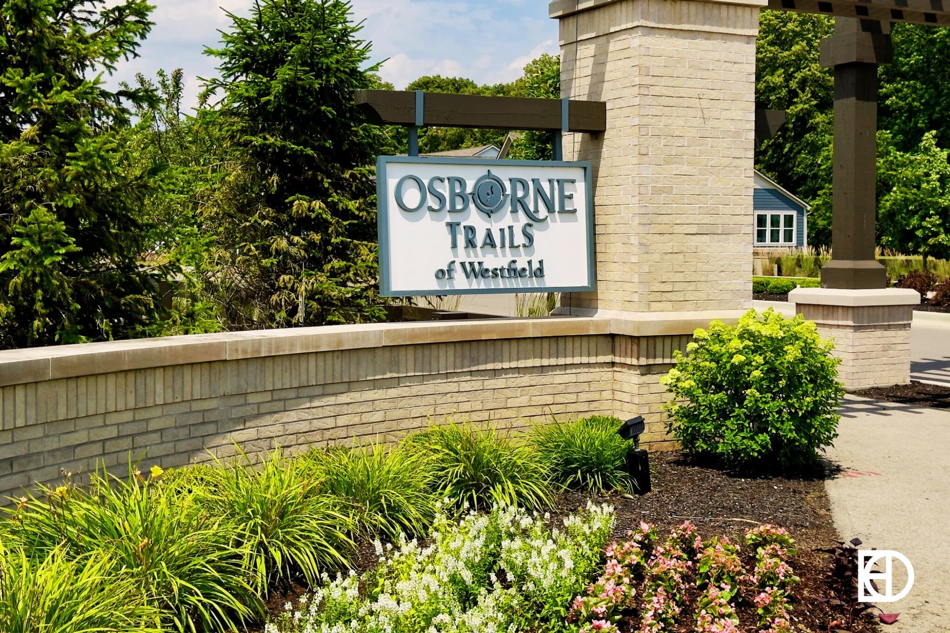 Photo of entrance sign of Osborne Trails of Westfield hanging on stone column attached to low stone wall with landscaping.