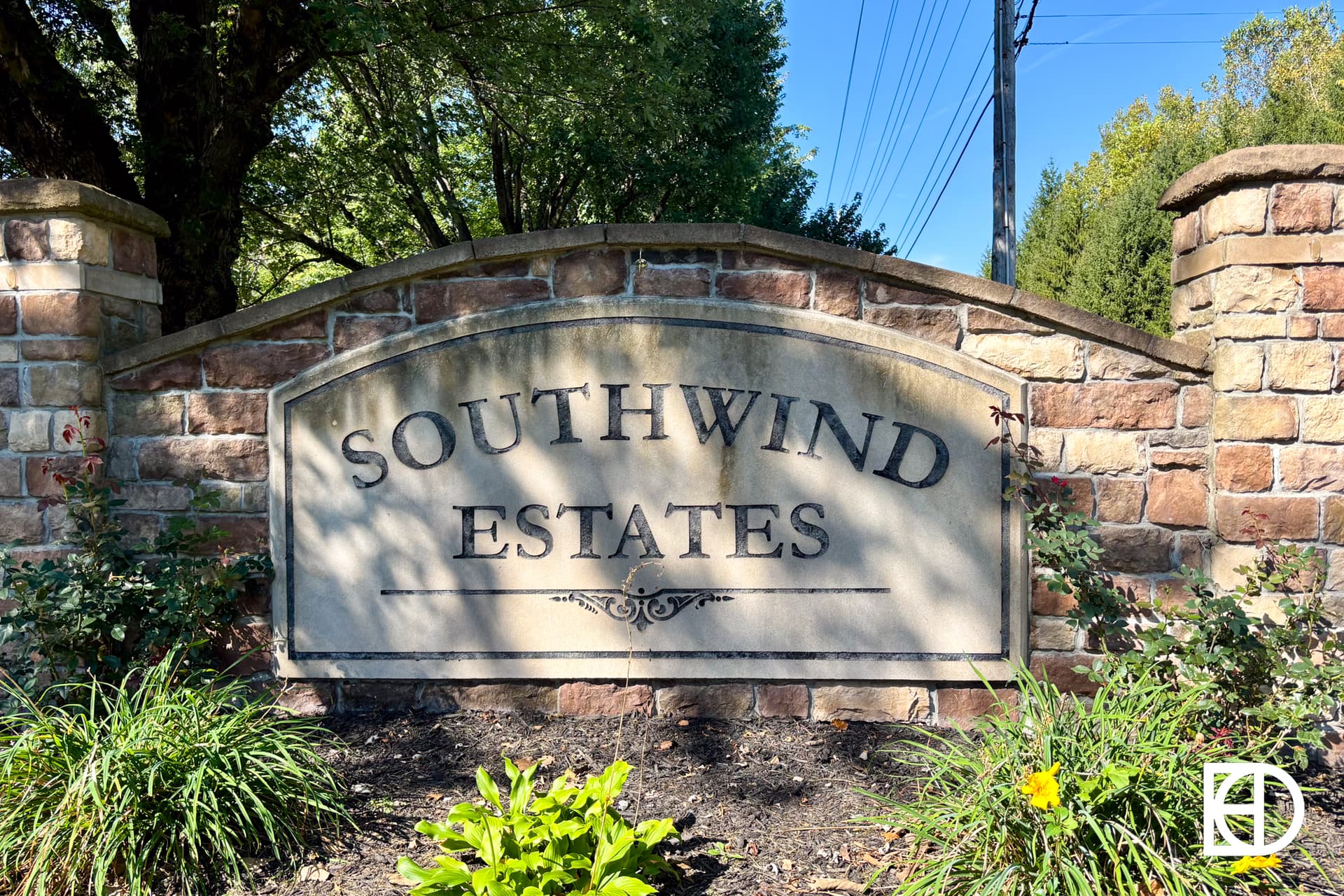 A stone entrance sign reads Southwind Estates, surrounded by greenery and flowers, with a brick wall and trees in the background.