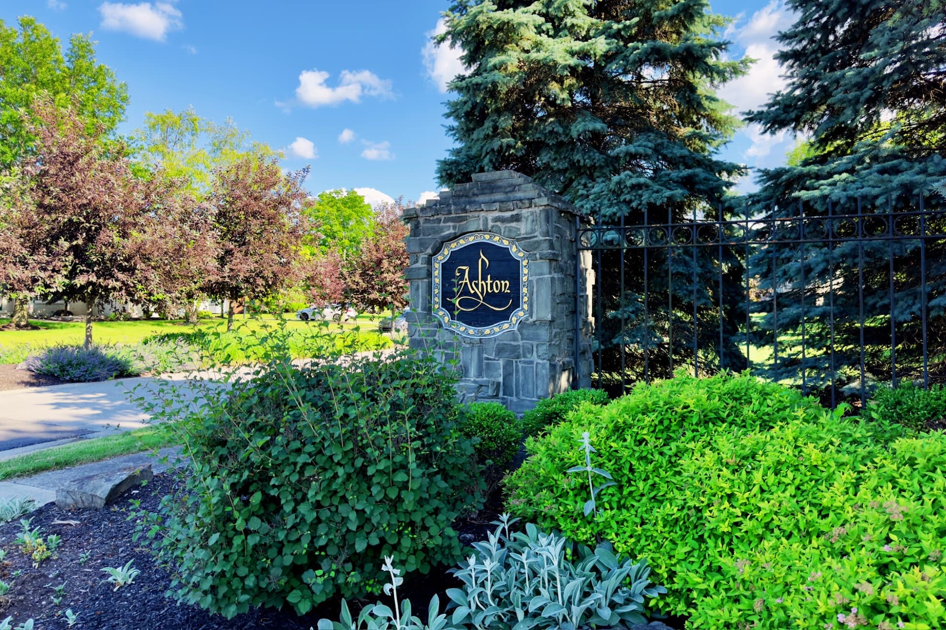Stone entrance sign to Ashton neighborhood with landscaping set amongst trees next to a tree-lined entrance.