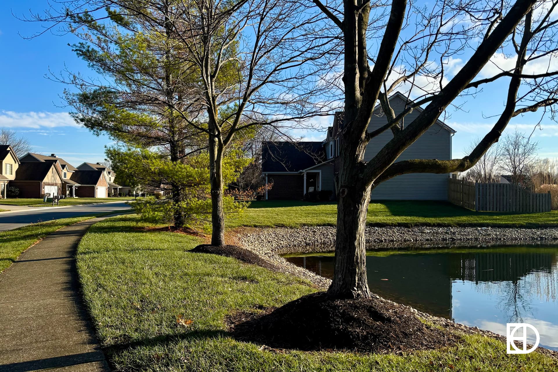 Exterior photo of Princeton/Harvard Park, showing sidewalk, homes, pond, and landscaping