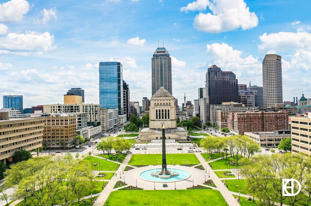 Aerial view of Indiana World War Memorial and Veterans' Memorial Plaza with downtown Indianapolis skyline behind.