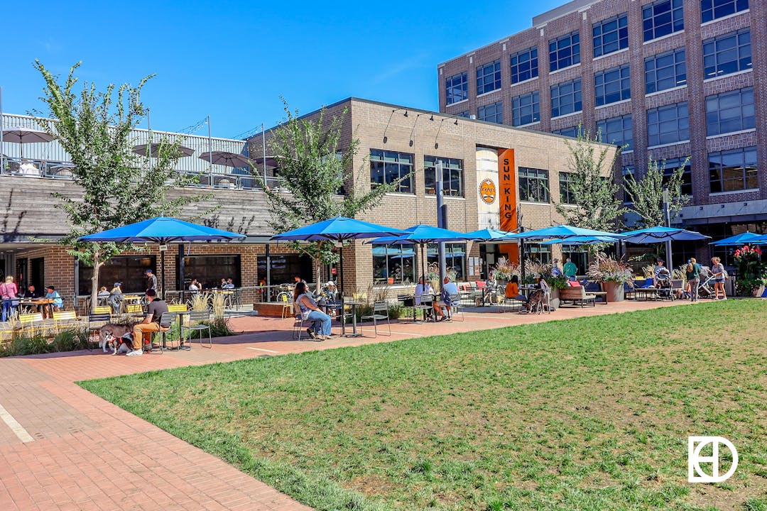 Exterior photo of Sun King Brewery and plaza, with exterior seating and turf lawn